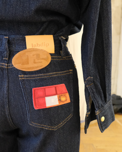 Jean en denim bleu foncé 100% coton avec coupe droite et détails de surpiqûres jaunes, matière épaisse et patchs discrets sur la poche arrière.