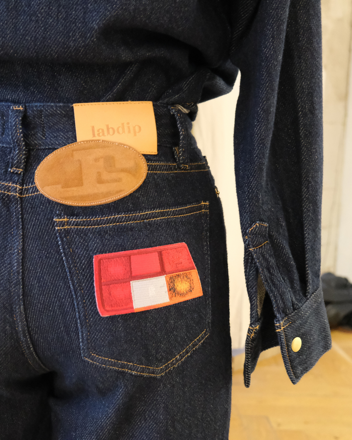 Jean en denim bleu foncé 100% coton avec coupe droite et détails de surpiqûres jaunes, matière épaisse et patchs discrets sur la poche arrière.