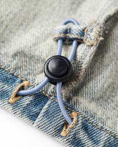 Gros plan sur un jean en denim bleu délavé avec cordon élastique réglable et bouton noir, matière 100 % coton, style décontracté et confortable pour femme.