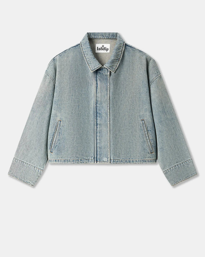 Veste en denim bleu clair effet délavé, coupe droite et légèrement courte avec poches latérales discrètes, matière coton épaisse et structurée.