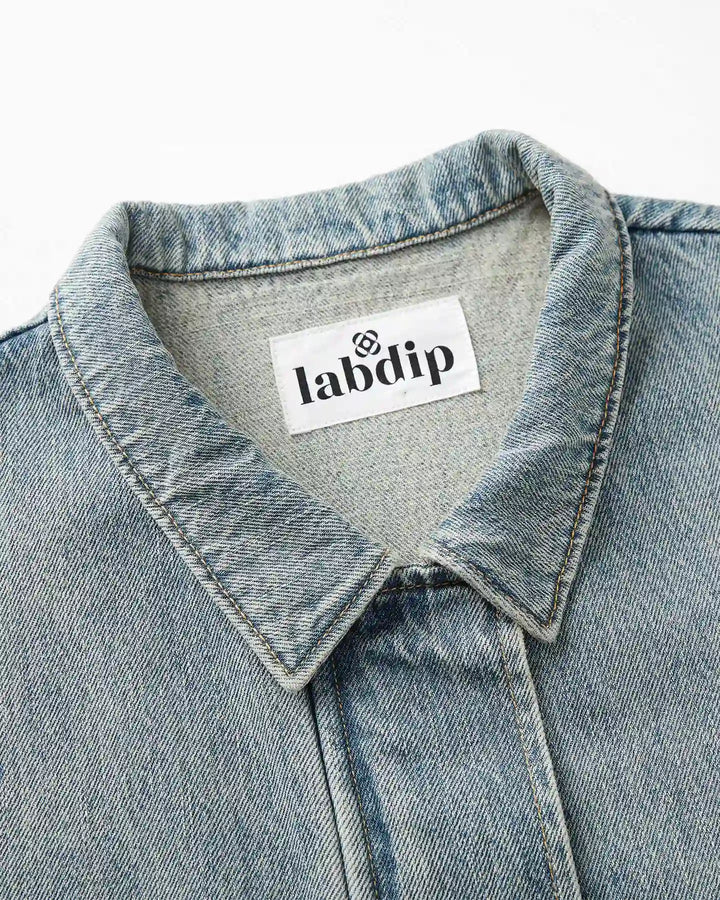 Détail du col d’une veste en denim bleu délavé avec couture apparente, tissu en coton robuste et étiquette de la marque Labdip.