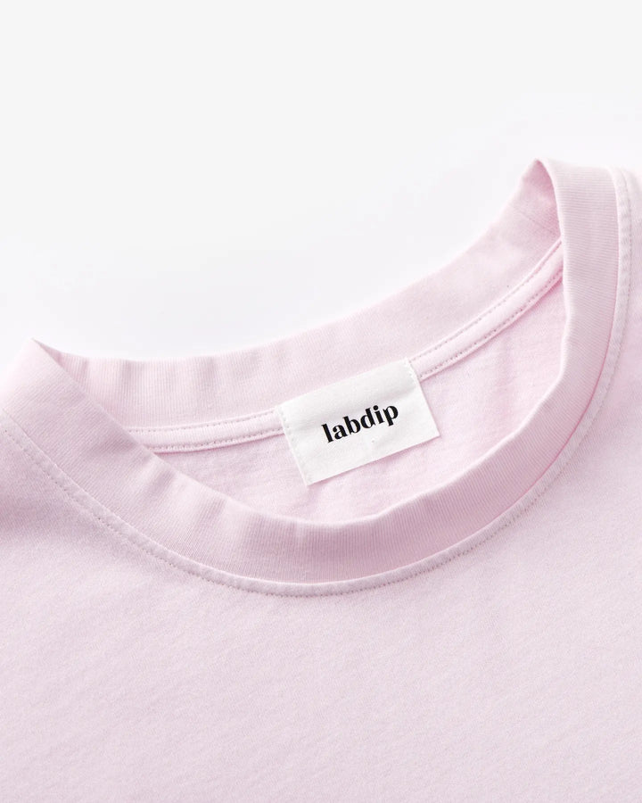 T-shirt en coton rose clair avec col rond et couture minimaliste, offrant un style simple et décontracté adapté à la saison estivale.