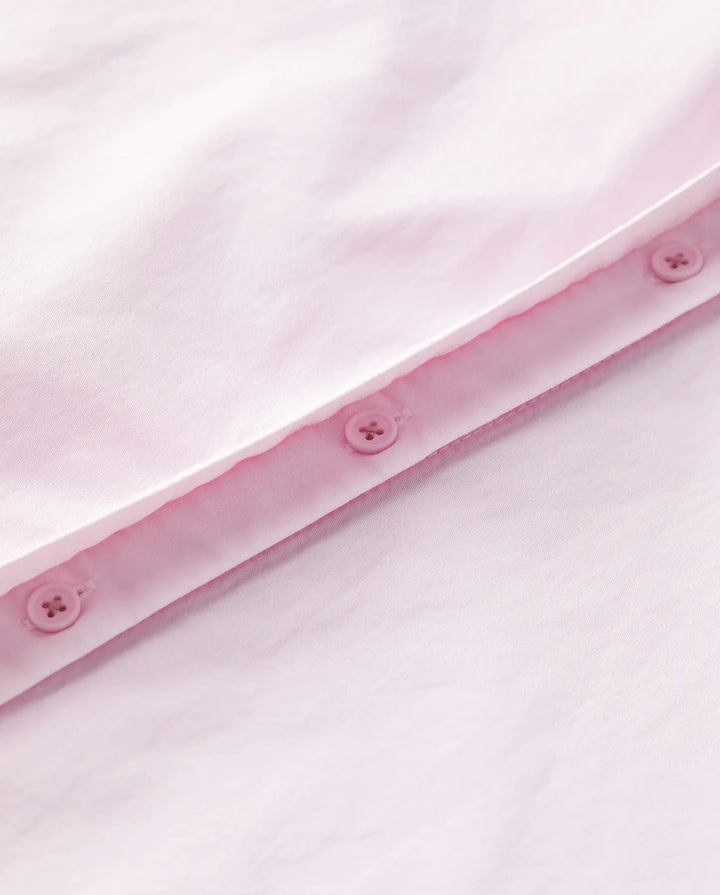 Détail d’un tissu popeline rose clair en coton, lisse et léger, avec une finition soignée comprenant des boutons assortis cousus sur une couture propre.