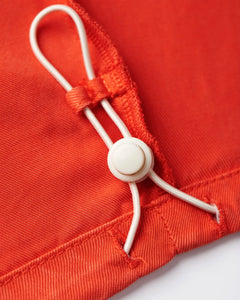 Détail fin en tissu tencel orange vif avec cordon réglable et bouton blanc, soulignant la qualité douce et la coupe ajustée du pantalon pour femme.