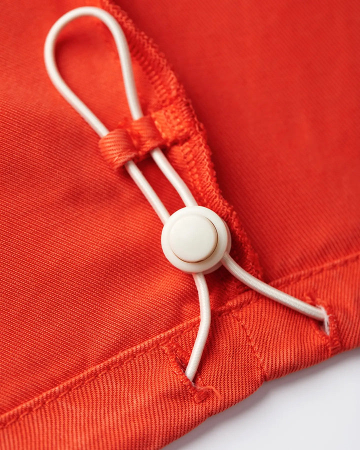 Détail fin en tissu tencel orange vif avec cordon réglable et bouton blanc, soulignant la qualité douce et la coupe ajustée du pantalon pour femme.