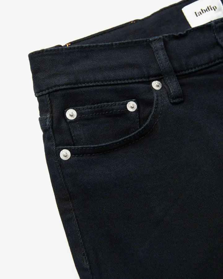 Jean femme en denim noir profond, coupe droite et ajustée, matière 100% coton, avec rivets métalliques et poche avant discrète pour un style élégant et confortable.