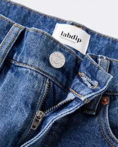 Gros plan sur un jean en denim bleu indigo avec fermeture éclair métallique et bouton argenté, coupe droite adaptée à toutes les morphologies féminines.