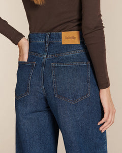Jean ballon en denim bleu moyen 100% coton avec taille haute et poches arrière carrées, conçu pour s'adapter à toutes les morphologies féminines.
Porté par le mannequin de dos