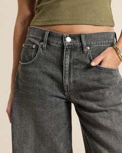 Jean femme en denim gris poussiéreux, coupe large et droite, tissu 100 % coton, avec poches avant et détails en rivets cuivrés, s'adaptant à toutes les morphologies.