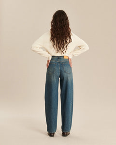 Jean en denim indigo avec finition légèrement délavée, coupe barrel et taille haute, offrant un tombé fluide et confortable parfaitement adapté à toutes les morphologies féminines.