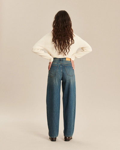 Jean en denim indigo avec finition légèrement délavée, coupe barrel et taille haute, offrant un tombé fluide et confortable parfaitement adapté à toutes les morphologies féminines.