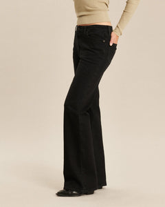 Jean femme en denim noir charbon avec coupe bootcut, matière douce et épaisse, ajusté aux hanches et évasé à partir du genou pour un style moderne et confortable.