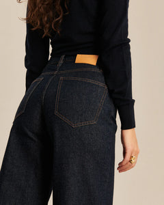 Jean femme en denim brut foncé, coupe large et légèrement ballon, matière 100% coton avec coutures contrastantes orange, adaptée à toutes les morphologies.
