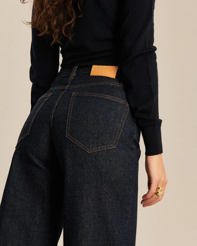 Jean femme en denim brut foncé, coupe large et légèrement ballon, matière 100% coton avec coutures contrastantes orange, adaptée à toutes les morphologies.