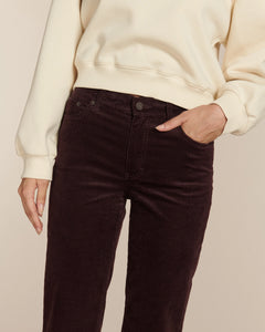 Jean en velours côtelé de couleur marron foncé, coupe droite avec taille haute, cintré aux hanches et légèrement évasé vers le bas, tissu doux et épais adapté à toutes morphologies.