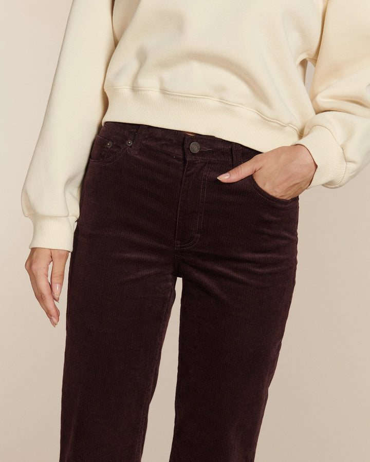Jean en velours côtelé de couleur marron foncé, coupe droite avec taille haute, cintré aux hanches et légèrement évasé vers le bas, tissu doux et épais adapté à toutes morphologies.