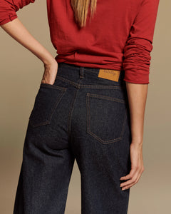Jean femme en denim brut 100% coton, coupe barrel ample et taille haute, couleur bleu foncé avec surpiqûres contrastées et étiquette en cuir "labdip".
Porté par le mannequin de dos