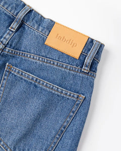 Jean en denim bleu clair 100% coton avec coupe droite et taille haute, finitions soignées et étiquette en cuir beige discrète.