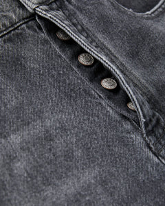 Détail rapproché d’un jean pour femme en denim gris poussière avec boutons métalliques apparents, matière 100 % coton au toucher robuste, coupe ajustée et confortable.
