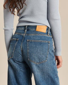 Jean femme en denim bleu moyen, coupe droite légèrement large, tissu 100% coton avec ceinture et poches arrière, style décontracté et confortable.
Porté par le mannequin de dos