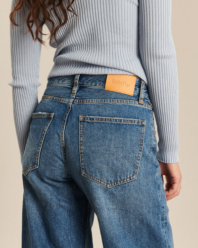 Jean femme en denim bleu moyen, coupe droite légèrement large, tissu 100% coton avec ceinture et poches arrière, style décontracté et confortable.
Porté par le mannequin de dos