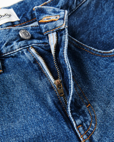 Jean en denim bleu moyen 100 % coton avec fermeture éclair, coupe droite et ajustée, coutures orange apparentes, idéal pour femme.