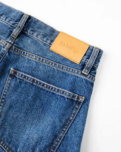 Jean femme en denim bleu moyen, 100 % coton, coupe droite et ajustée avec étiquette en cuir beige, offrant un maintien confortable et un style intemporel.