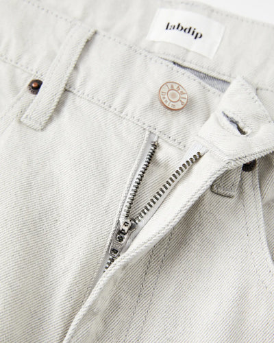 Jean pour femme en denim non teinté couleur granit clair, coupe droite avec fermeture éclair et bouton métal gravé, confection 100% coton avec finition sobre et naturelle.