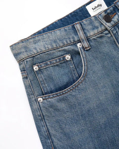 Jean femme en denim bleu clair délavé, coupe droite avec poches classiques renforcées par rivets métalliques, tissu en coton épais et confortable, idéal pour l'été.