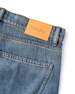 Jean en denim bleu légèrement délavé, coupe droite classique avec poche arrière, ceinture renforcée et étiquette en cuir avec logo Labdip.