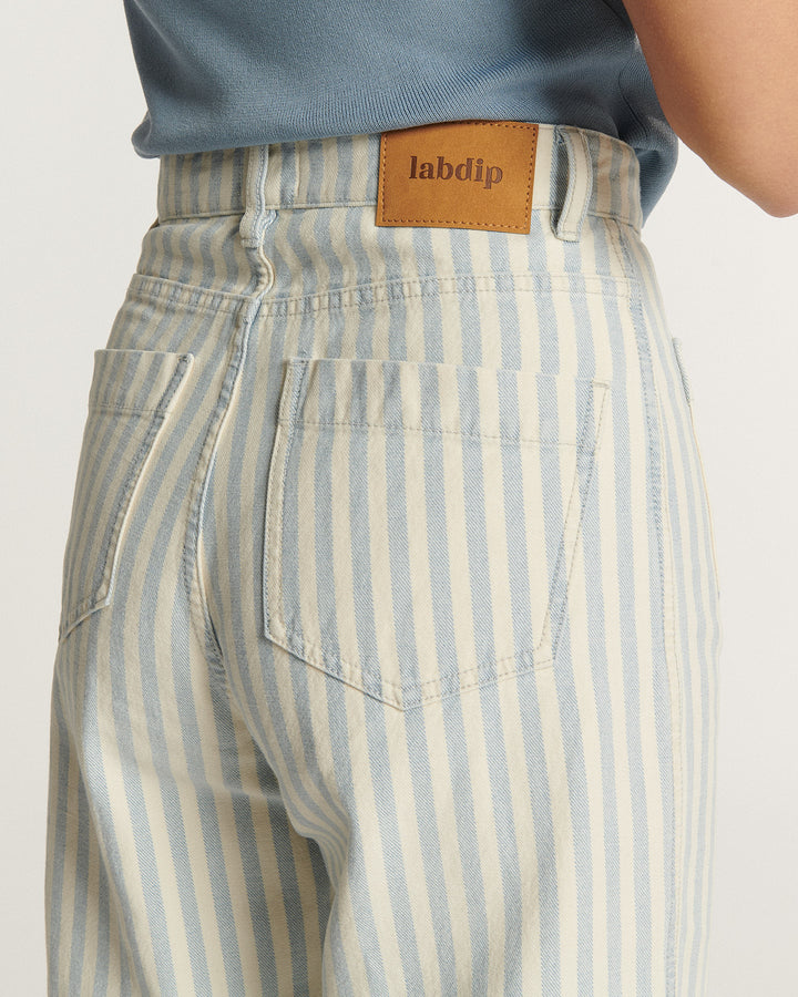Jean 100 % coton pour femme avec rayures bleu clair et écru, coupe droite offrant un ajustement confortable et moderne, étiquetage en cuir naturel.