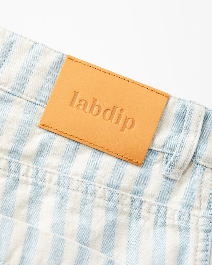 Détail d'un jean en denim rayé bleu clair et blanc en coton avec une étiquette cuir camel embossée Labdip, coupe droite adaptée à toutes morphologies féminines.