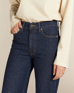 Jean droit long en denim brut bleu foncé 100 % coton avec taille haute et coutures contrastantes, s’adaptant parfaitement à toutes les morphologies féminines.
porté par le mannequin de face